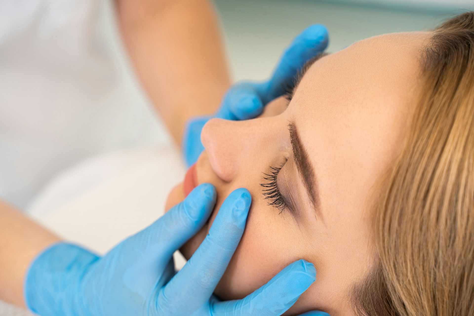 Practitioner in blue gloves examining a woman's face during a skincare treatment.